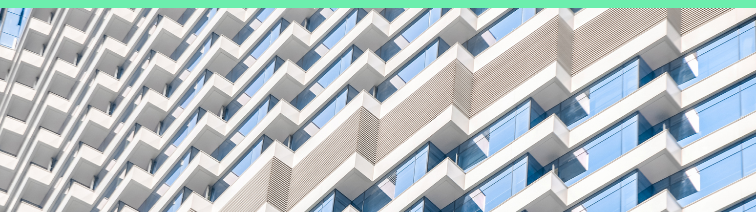 The image shows a modern high rise building with a strong geometric facade. Rows of balconies and large glass windows create a repeating pattern across the structure. The perspective emphasizes diagonal lines and symmetry, giving the architecture a dynamic, abstract quality. Soft, neutral tones and blue-tinted glass contribute to a clean, contemporary aesthetic.