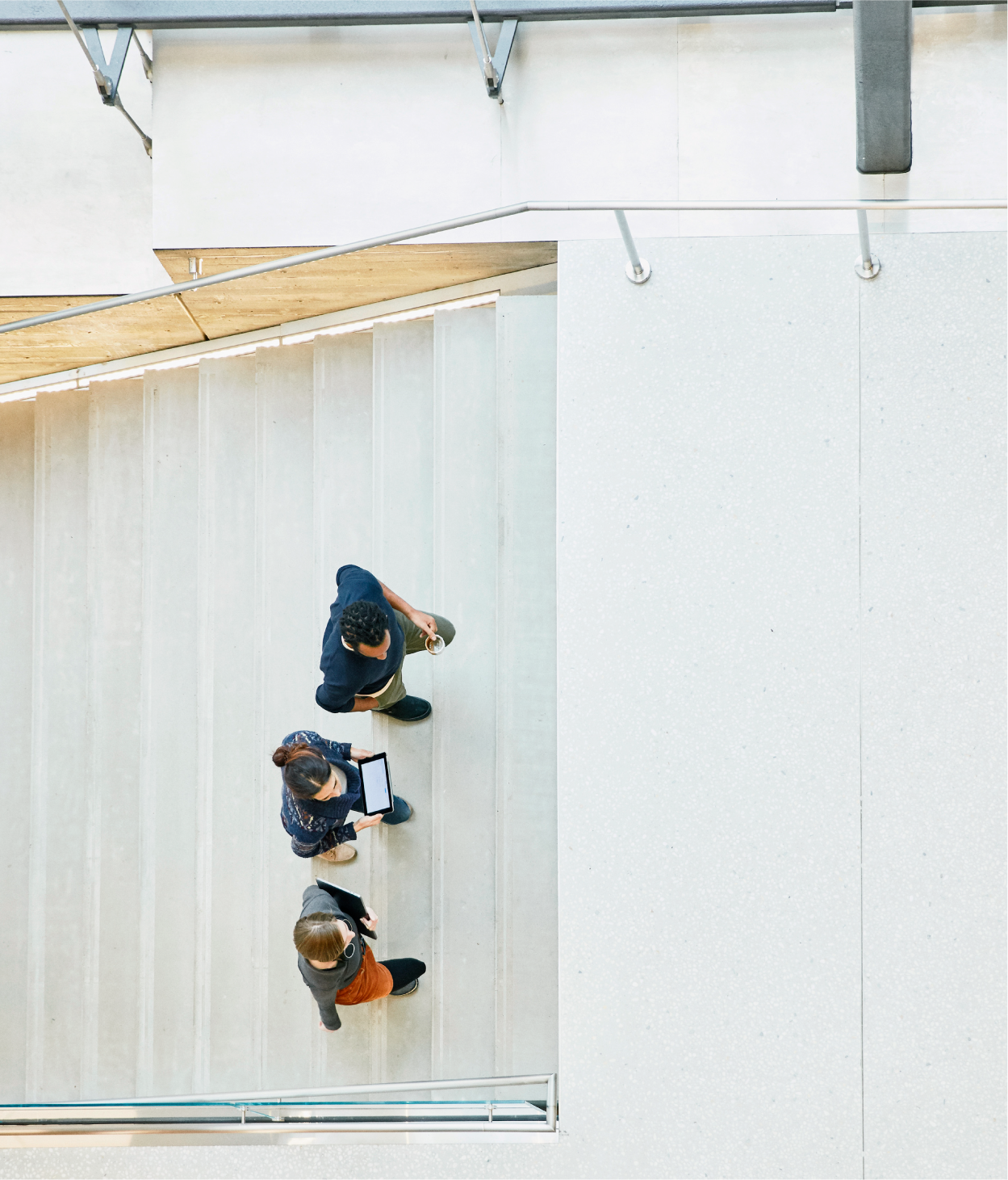aerial overhead photo of three coworkers conversing as they climb a set of office lobby stairs.